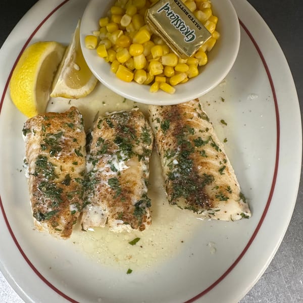 Three fish fillets with herbs, lemon wedges, and a side of corn with Grassland butter.