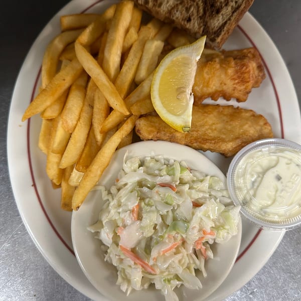 Plate of fish and chips with coleslaw, a lemon wedge, tartar sauce, and dark bread.